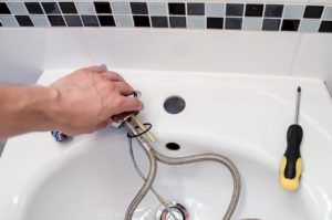 Eine Person hält eine Armatur in der Hand, während sie das Waschbecken montiert. Auf dem Rand liegt ein Schraubendreher.