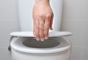 Eine Hand hält einen weißen WC-Deckel fest. Es schein kein Toilettendeckel mit Absenkautomatik zu sein.